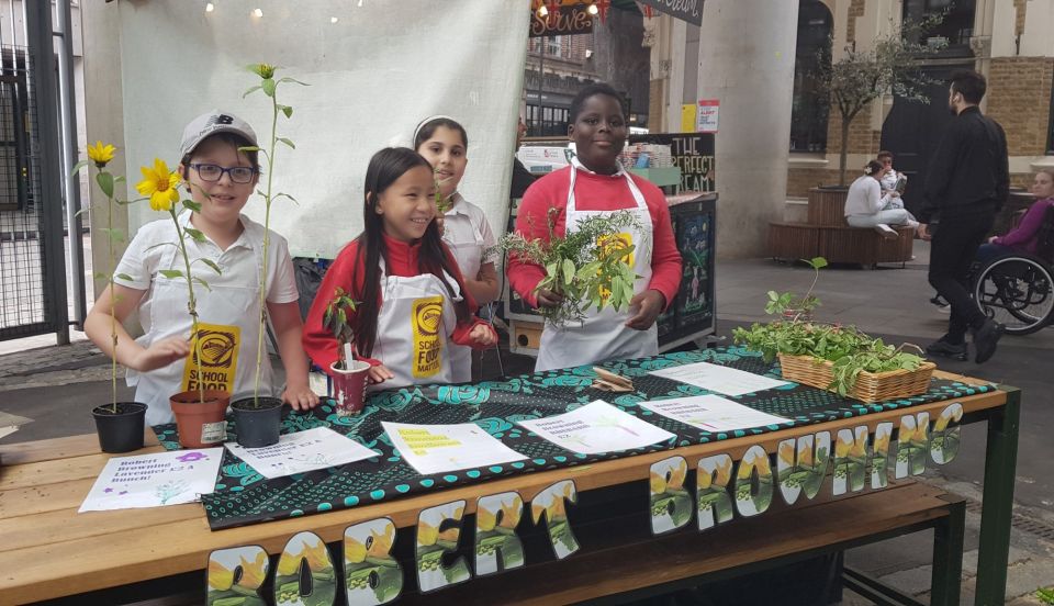 A table with a sign that reads 'Robert Browning' , with homegrown vegetables on it and four pupils smiling behind it.