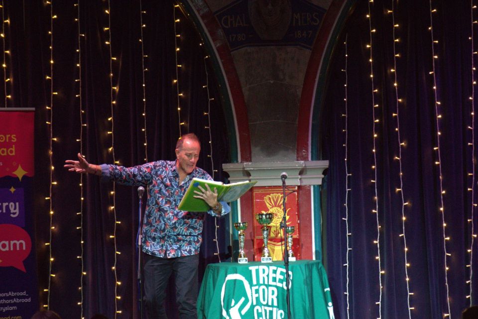 Poet Chris White performing on stage, book in hand