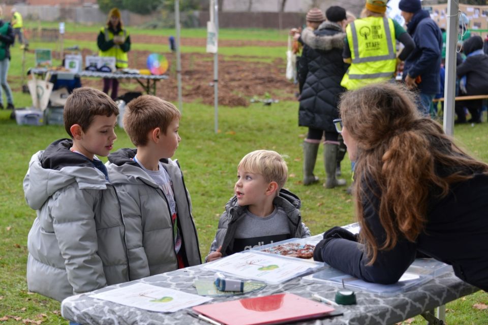 3 children at a planting day talking to an adult volunteer at a table