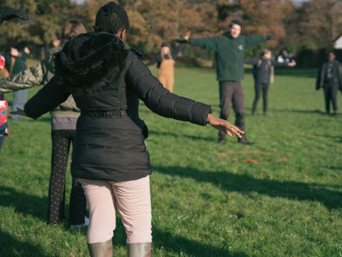a group of people standing in a field doing warm up yoga exercises, casting long shadows on the grass