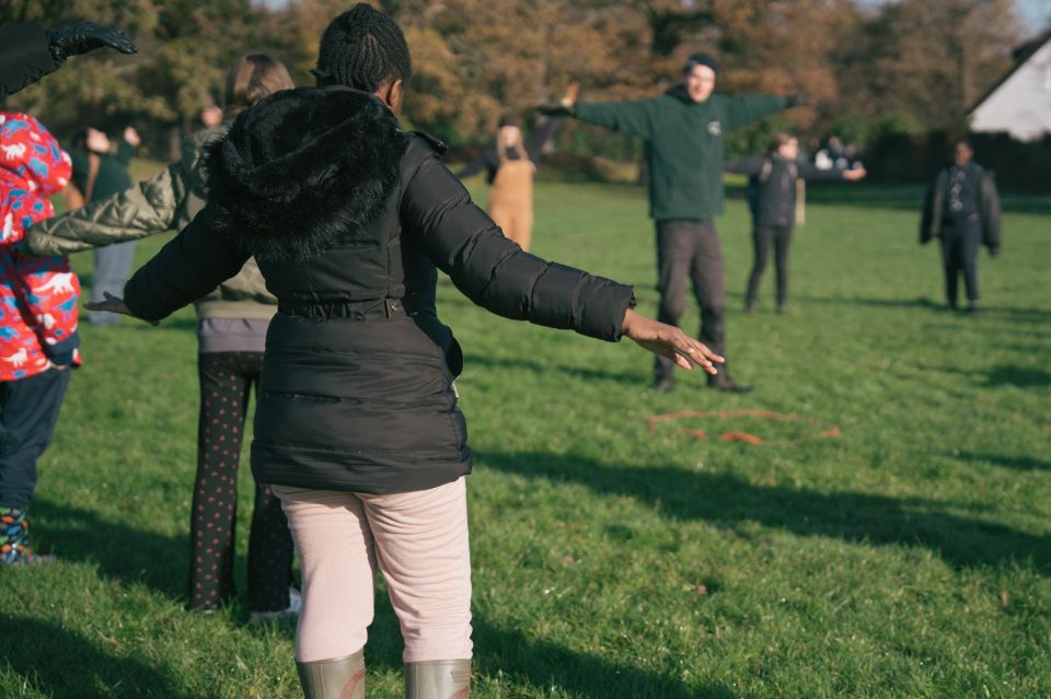 a group of people standing in a field doing warm up yoga exercises, casting long shadows on the grass